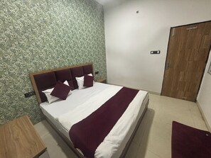 A neatly made bed with a wooden headboard, a wooden nightstand, and a wooden door. - Hotel Dev Shree Palace (Ujjain)