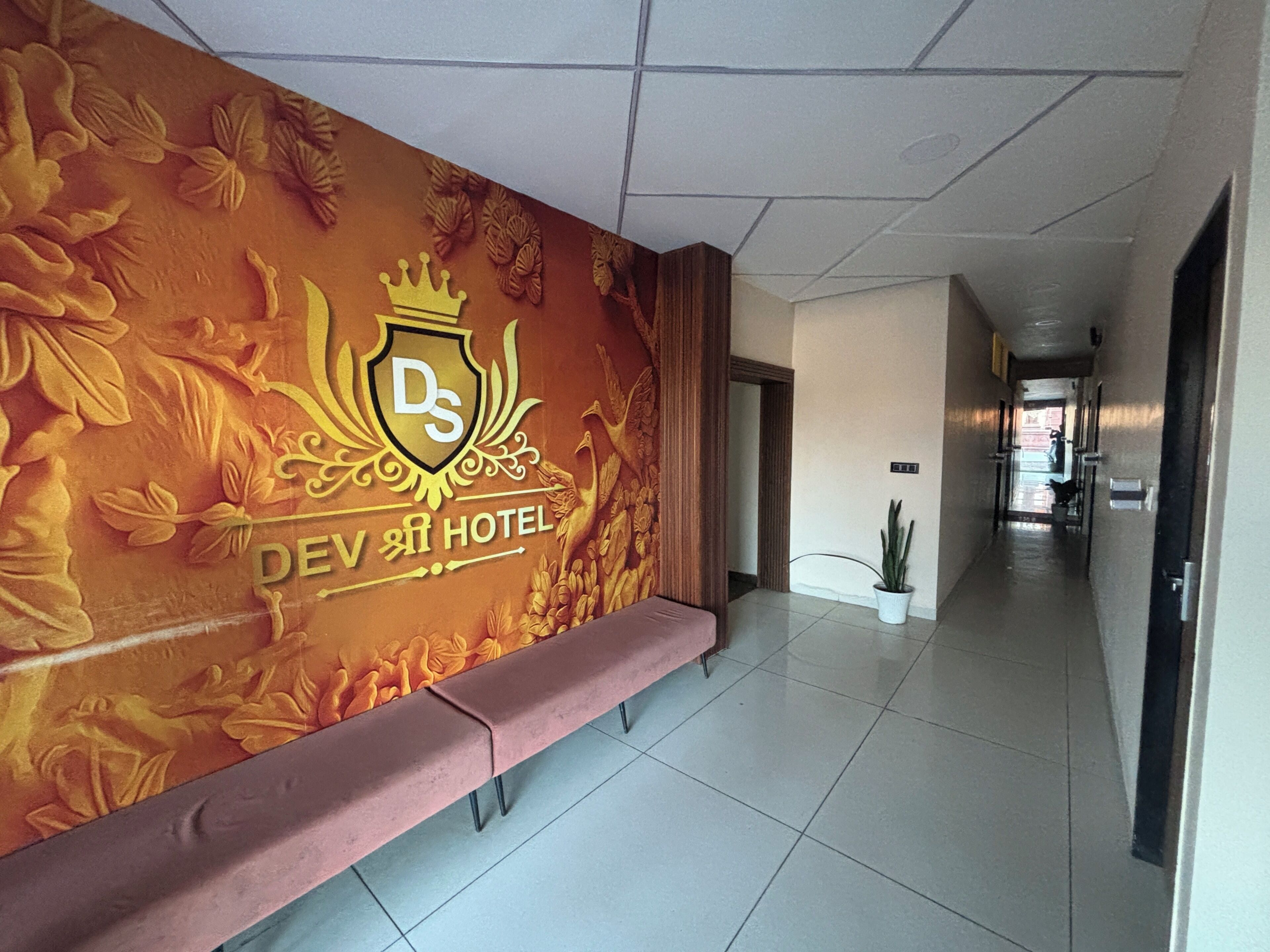 Un vestíbulo de hotel con un largo pasillo, un banco y una pared con un logotipo y un diseño floral.