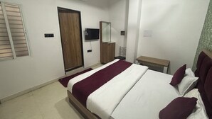 A bedroom with a bed, a TV, a wooden wardrobe, a mirror, and a small table. - Hotel Dev Shree Palace (Ujjain)