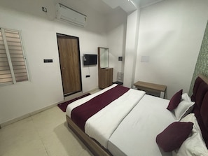 A bedroom with a bed, a TV, a wooden wardrobe, a mirror, and a small table. - Hotel Dev Shree Palace (Ujjain)