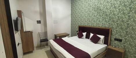 A bedroom with a bed, a chair, a bedside table, a ceiling fan, and a wall with a leafy pattern.