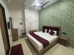 Quarto com cama, cadeira, mesa de cabeceira, ventoinha no teto e parede com padrão de folhagem.
