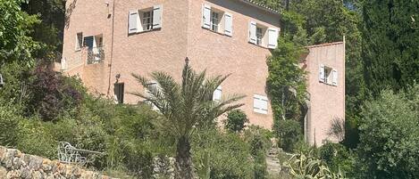 A two-story building with a swimming pool, surrounded by greenery and a stone wall.
