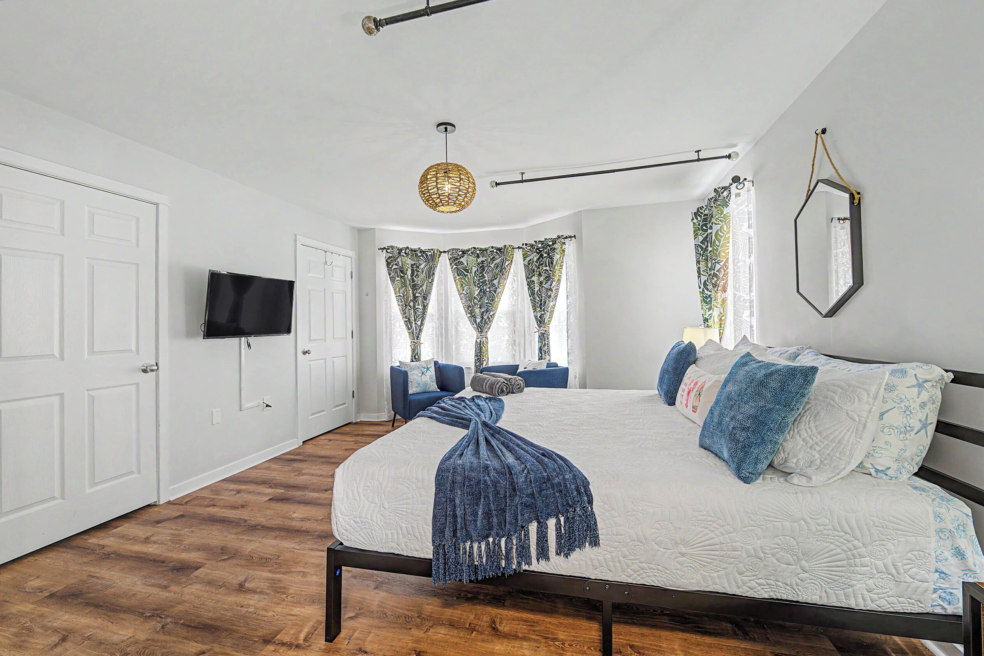 A bedroom with a bed, a television, a window with curtains, and a hanging light fixture.