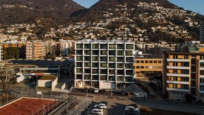 Un edificio moderno caratterizzato da una facciata a griglia di finestre, circondato da un'area parcheggio e un campo da basket.