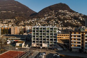 A modern building with a grid of windows, surrounded by a parking area and a basketball court. - {Suite 412} Gym, Business Room, Modern, Relax (Lugano)