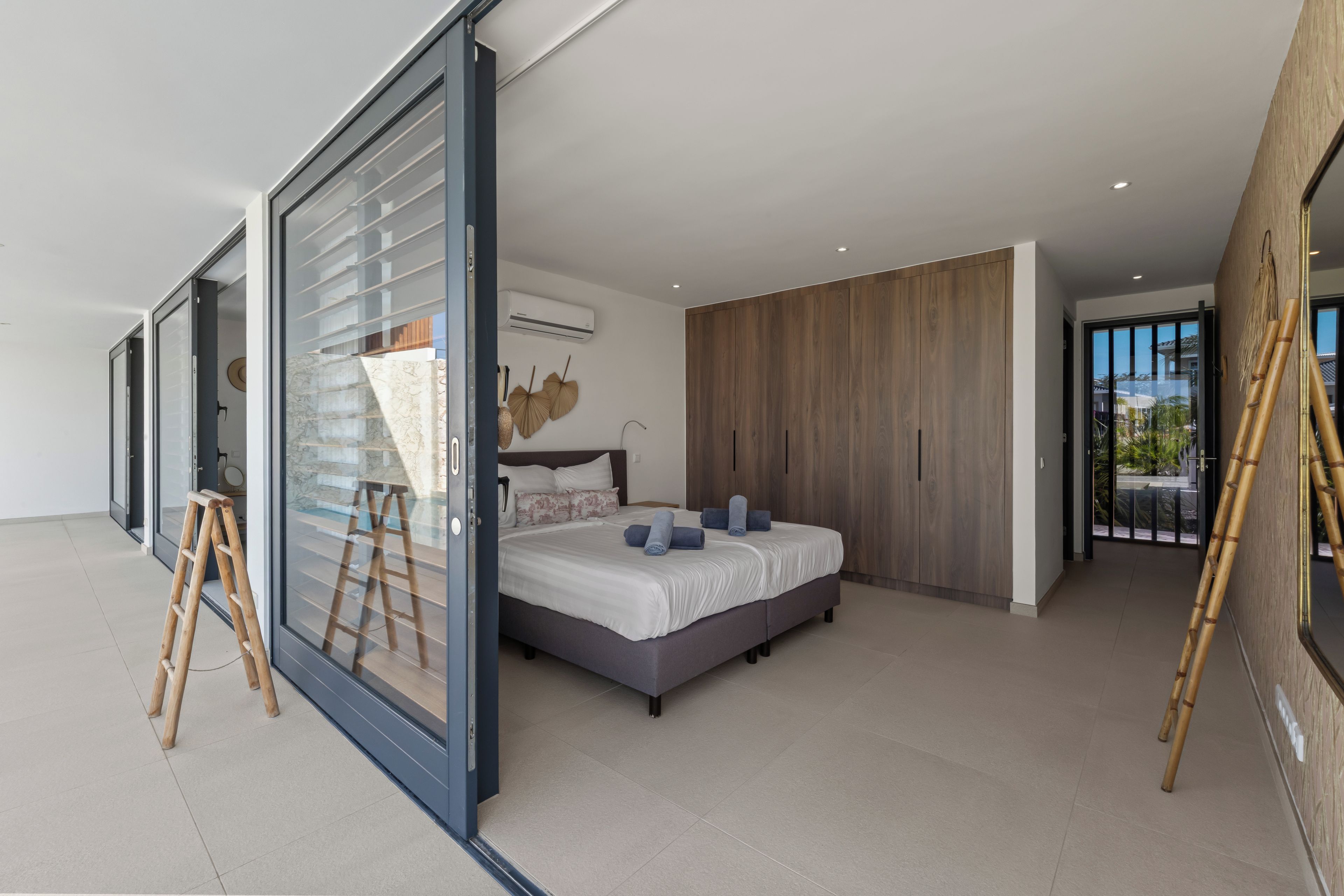 Een moderne slaapkamer met een groot bed, een schuifglasdeur naar een balkon en uitzicht op de omgeving.