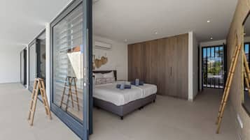 Een moderne slaapkamer met een groot bed, een schuifglasdeur naar een balkon en uitzicht op de omgeving.