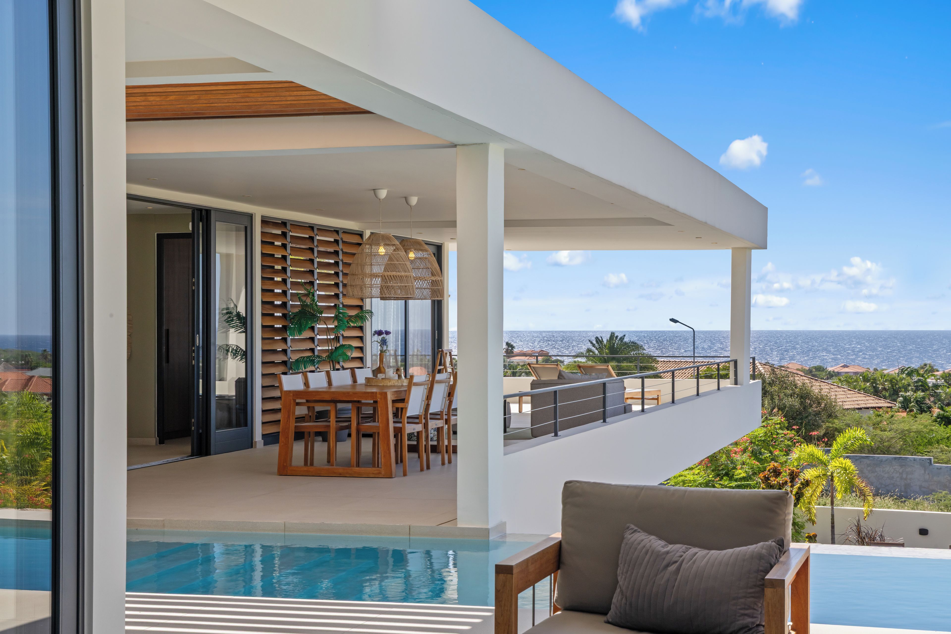 A modern outdoor dining area with a pool, overlooking a coastal view.