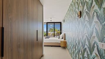 A bedroom with a bed, a wooden wardrobe, a ceiling fan, and a window with a view of greenery.