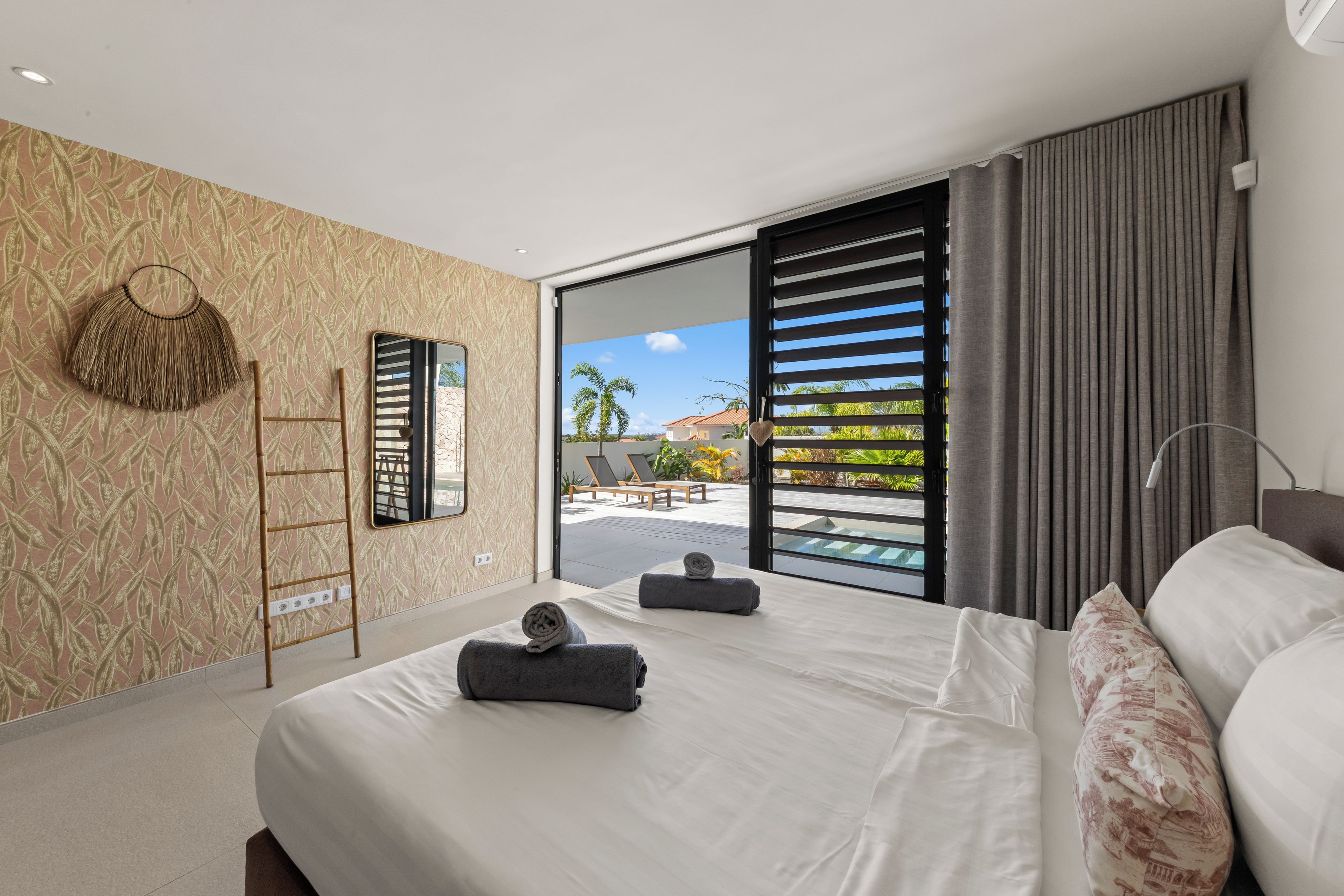 A modern bedroom with a large bed, a view of the outdoors, and a balcony with a pool.