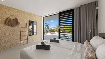 A modern bedroom with a large bed, a view of the outdoors, and a balcony with a pool.