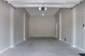 Een schone, lege gang met witte muren en een betonnen vloer, die naar een deur aan het einde leidt.