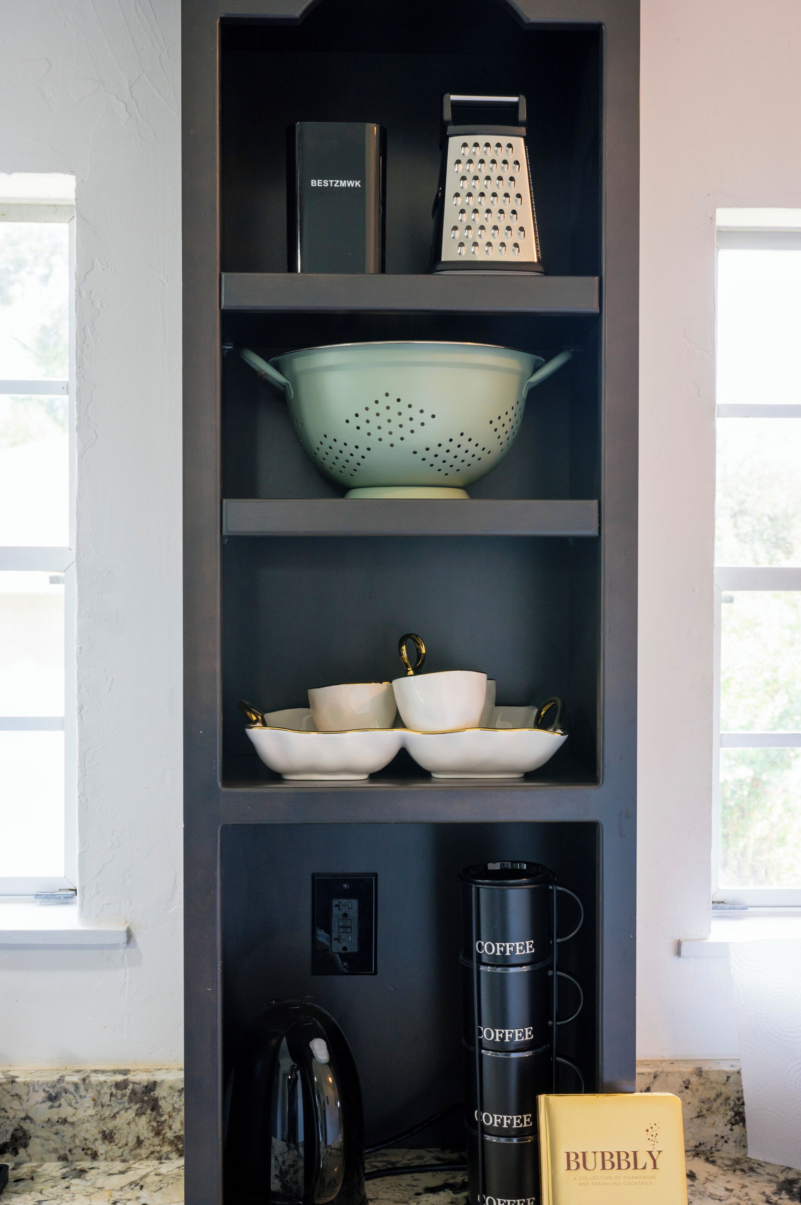 A kitchen with shelves holding kitchenware, a coffee maker, and a book.