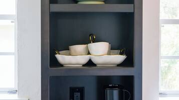 A kitchen with shelves holding kitchenware, a coffee maker, and a book.