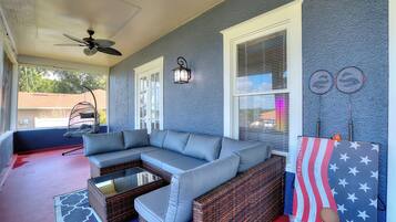 A covered porch with a sectional sofa, wicker furniture, a ceiling fan, and a wall-mounted lamp.