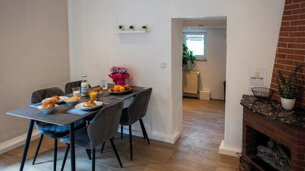 Uma sala de jantar com mesa posta para o café da manhã, lareira de tijolos e vista para a cozinha.