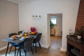 A dining area with a table set for breakfast, a brick fireplace, and a view into the kitchen. - Fireside by Loftigo - Terrace, Garden & Fireplace (Übach-Palenberg)