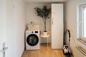 A laundry area with a washing machine, a drying basket, a potted plant, and a vacuum cleaner. - Fireside by Loftigo - Terrace, Garden & Fireplace (Übach-Palenberg)