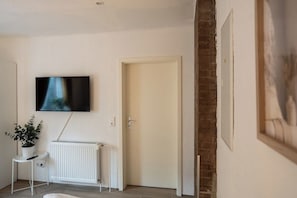 A room with a white radiator, a television mounted on the wall, a door, and a framed picture on the wall.