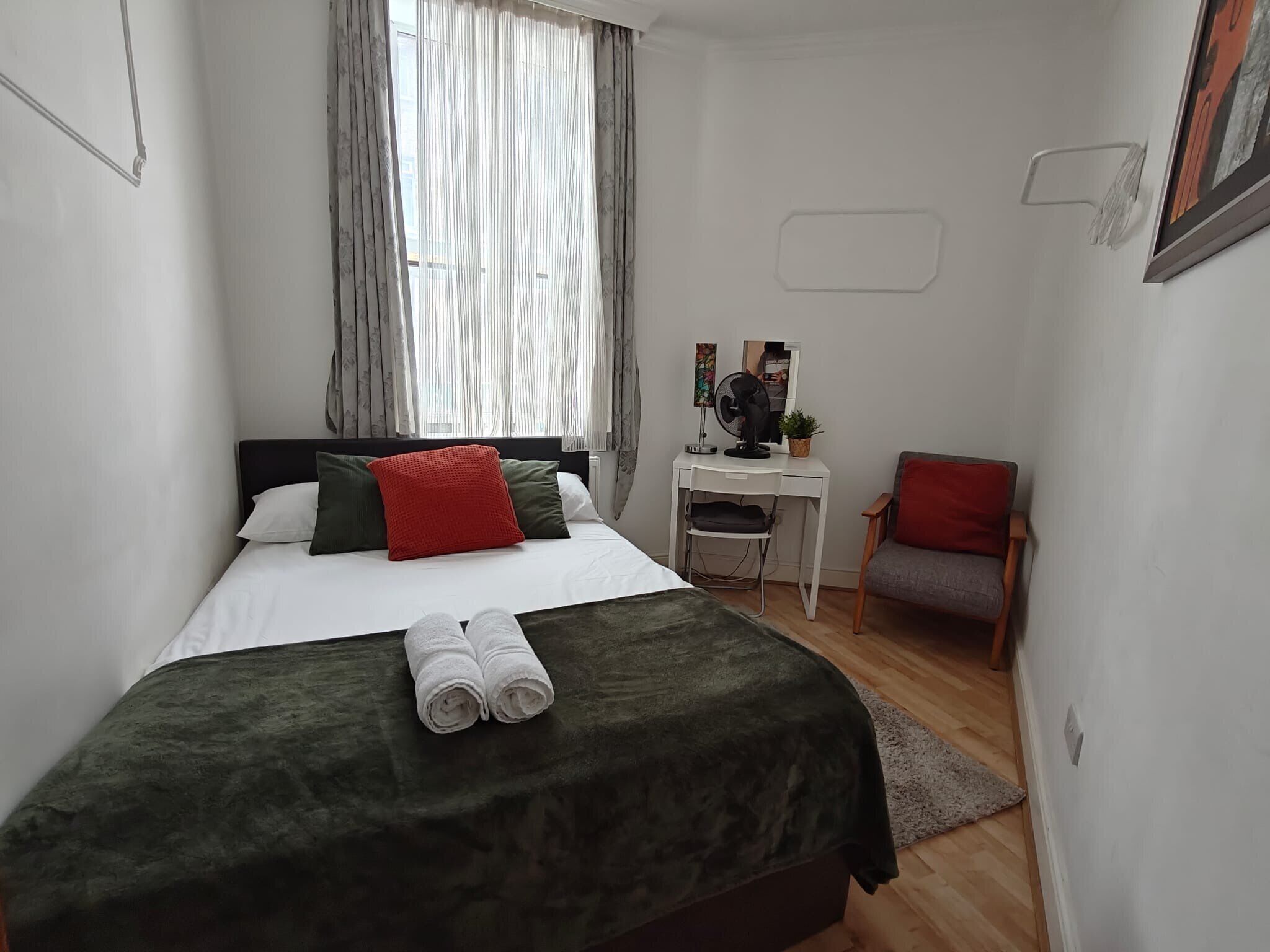 A bedroom with a bed, a desk, a chair, and a window with curtains.