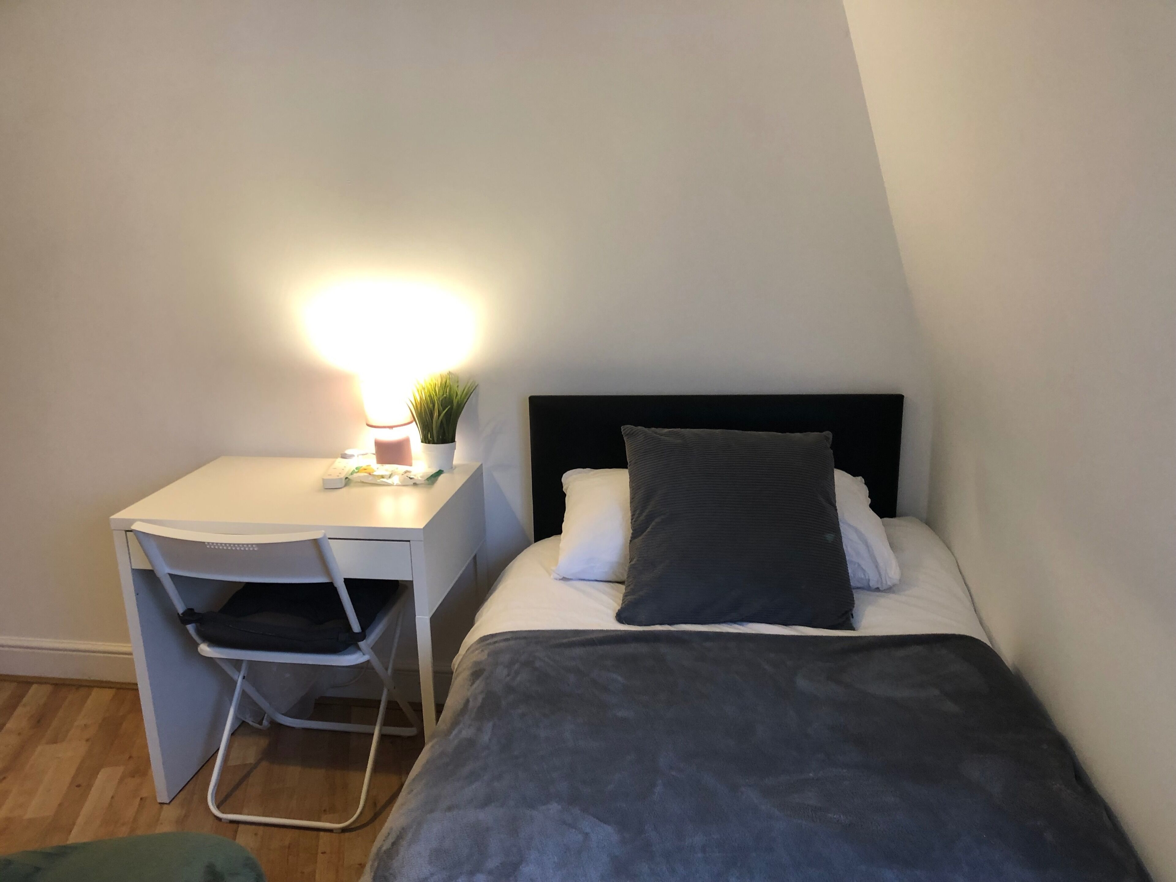 Ein kleines, ordentliches Schlafzimmer mit einem Bett, einem Schreibtisch und einem Stuhl.
