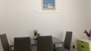 Ein Essbereich mit Tisch, vier Stühlen, einem gerahmten Bild an der Wand, einer kleinen Pflanze auf dem Tisch und einer grünen Kommode mit Schubladen.