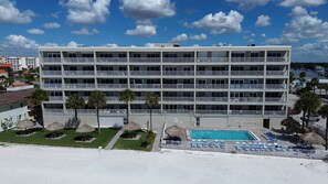 A multi-story hotel with a pool area, including lounge chairs and umbrellas. - 🌞Beachfront Condo🌴Sunset Views | Heated Pool + Tennis | Sea Oats 303 (Redington Shores)