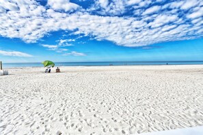 A sandy beach with footprints and a green umbrella. - 🌞Beachfront Condo🌴Sunset Views | Heated Pool + Tennis | Sea Oats 303 (Redington Shores)