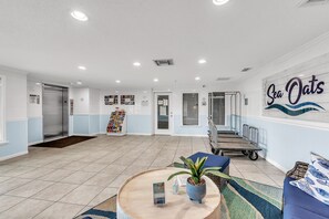 A reception area with a blue and white color scheme, a wall sign reading "Sea Oats," a reception desk, a seating area with a round table and chairs, and a small plant. - 🌞Beachfront Condo🌴Sunset Views | Heated Pool + Tennis | Sea Oats 303 (Redington Shores)