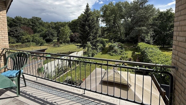 A balcony with a view of a landscaped garden, a chair, and a small table. - Garden Retreat by Loftigo - Balcony & Natural Serenity (Selfkant)