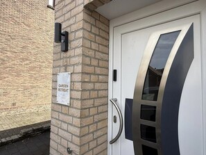 Eine Tür mit Metallbeschlag und Glasfenster, eine Ziegelwand und ein Schild mit der Aufschrift 'GARDEN RETREAT'.
