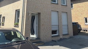A two-story residential building with a brick facade, a garage door, and a parked car. - Garden Retreat by Loftigo - Balcony & Natural Serenity (Selfkant)