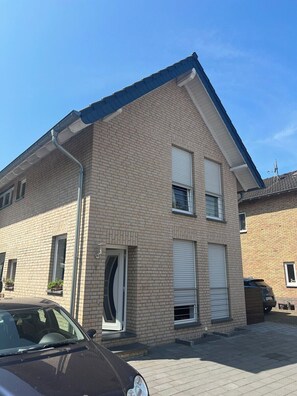 Een woonhuis met twee verdiepingen, een gevel van baksteen, een garagepoort en een geparkeerde auto.