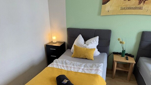 Une chambre d’hôtel avec un lit, une table de chevet avec une lampe, une petite table en bois avec un vase et un tableau au mur.