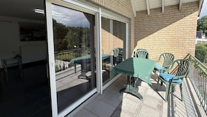 A covered patio with a table and chairs, a sliding glass door leading to an indoor area, and a brick wall. - Garden Retreat by Loftigo - Balcony & Natural Serenity (Selfkant)