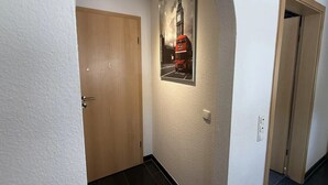 Un couloir avec une porte en bois, un tableau encadré représentant un autobus à deux étages rouge, et un mur blanc.