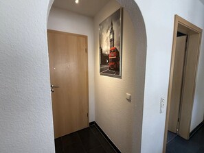 Ein Flur mit einer Holztür, einem gerahmten Bild eines roten Doppeldeckerbusses und einer weißen Wand.