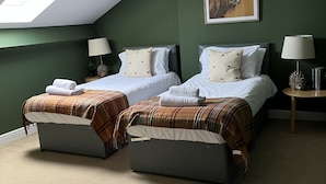 A bedroom with two beds, a skylight, a painting, and a small table with a lamp. - Exclusive Apartment at Historic Hall With Hard Tennis Court (Tadcaster)