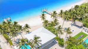 An aerial view of a beach resort with a swimming pool, palm trees, and a pier.