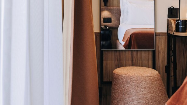 A hotel room with a bed, a bedside table, a mirror, a red wall light, and a brown curtain. - 705 O'Porto Hotel (Porto)