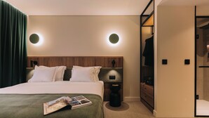 A modern hotel room with a large bed, a wooden headboard, two bedside lamps, a green curtain, a magazine on the bed, and a walk-in closet with a mirror. - 705 O'Porto Hotel (Porto)