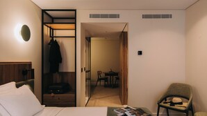 A hotel room with a bed, a seating area with a chair and a table, a coat rack, and a suitcase. - 705 O'Porto Hotel (Porto)
