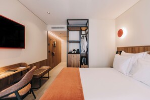 A hotel room with a bed, a desk, a chair, a coat rack, and a television. - 705 O'Porto Hotel (Porto)