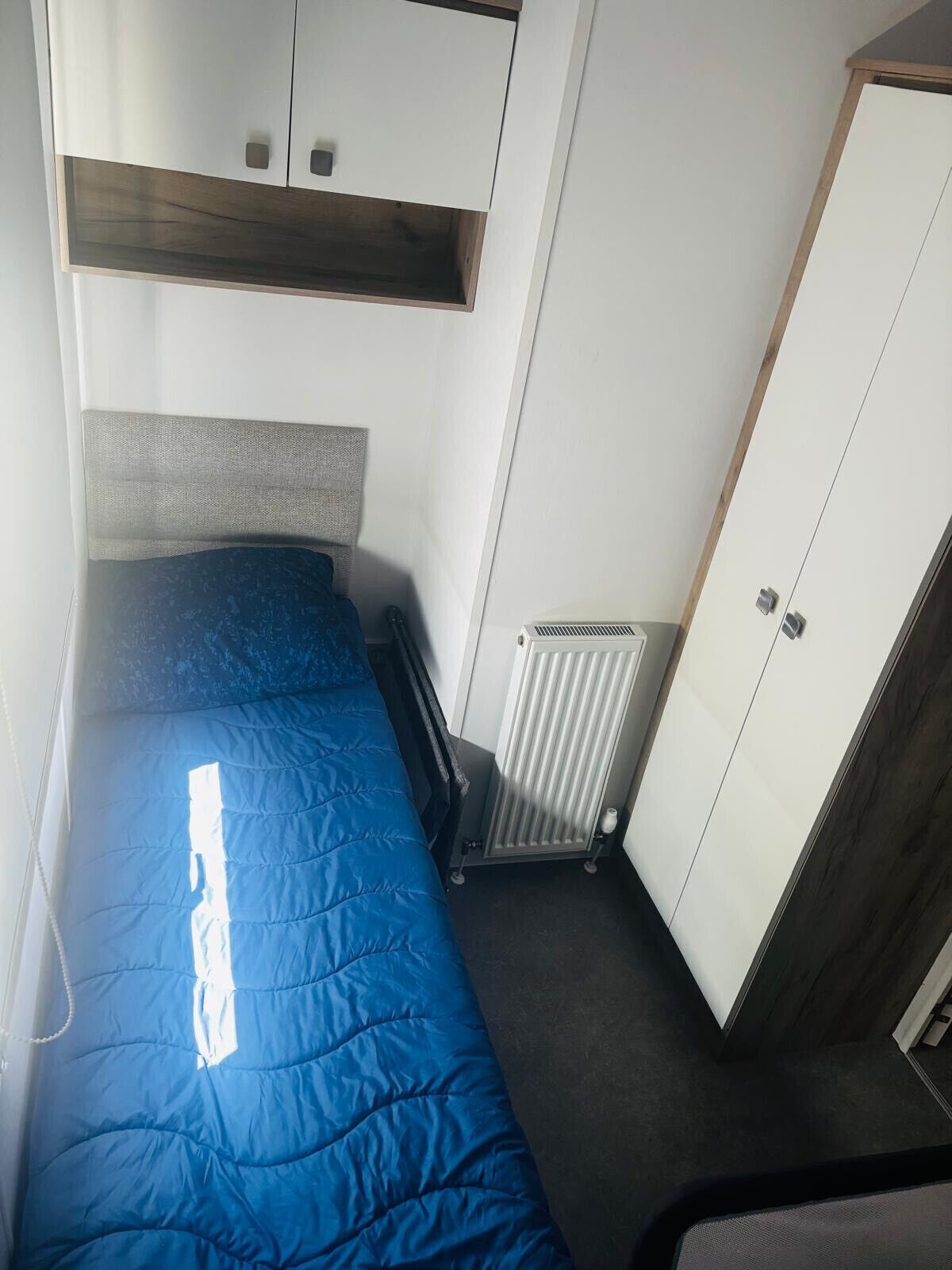 Een kleine, compacte kamer met een enkel bed, een kledingkast en een radiator.