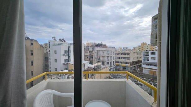 A balcony with a white chair and table, overlooking a cityscape with various buildings. - Larnaca Sunset One-bedroom Suite Close to the Beach (Larnaca)