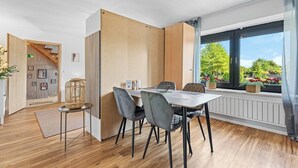 A modern dining area with a table and chairs, a wooden partition, and a window with a view of greenery. - Oasis by Loftigo - Cozy Apartment with Rain Shower (Selfkant)