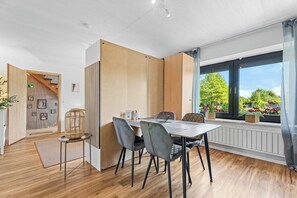 Een moderne eetruimte met een tafel, stoelen, een houten scheiding en een raam met uitzicht op groen.