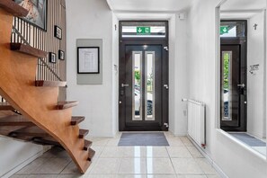 Ein modernes Interieur mit einer Holztreppe, einer schwarzen Tür mit grünem Fluchtzeichen und einem gerahmten Zertifikat an der Wand.
