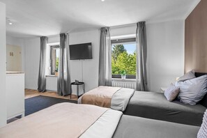 Habitación de hotel con dos camas, televisión, ventana con cortinas y vista a la vegetación.